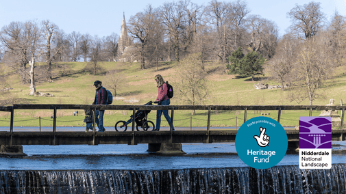 2 adults with a toddler and pushchair going across a bridge over a weir